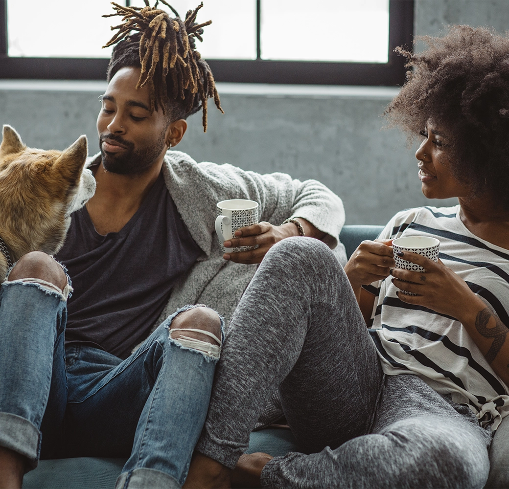 Couple on couch drinking coffee and petting their dog