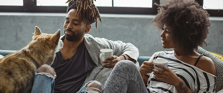 Couple on couch drinking coffee and petting their dog