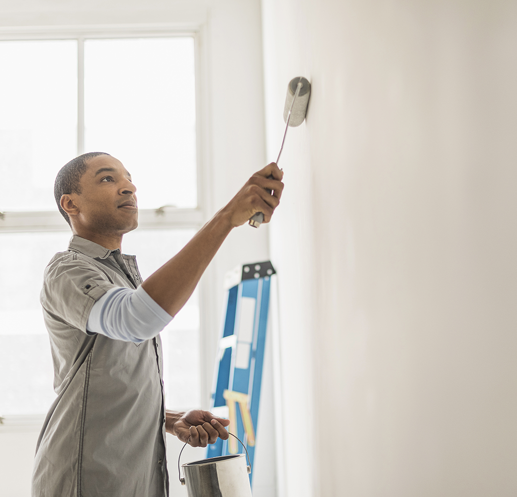 Black man with rolling brush in hand painting a wall inside a house