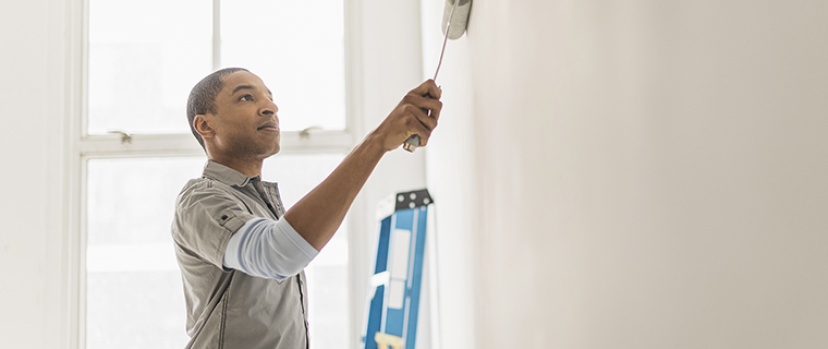 Black man with rolling brush in hand painting a wall inside a house