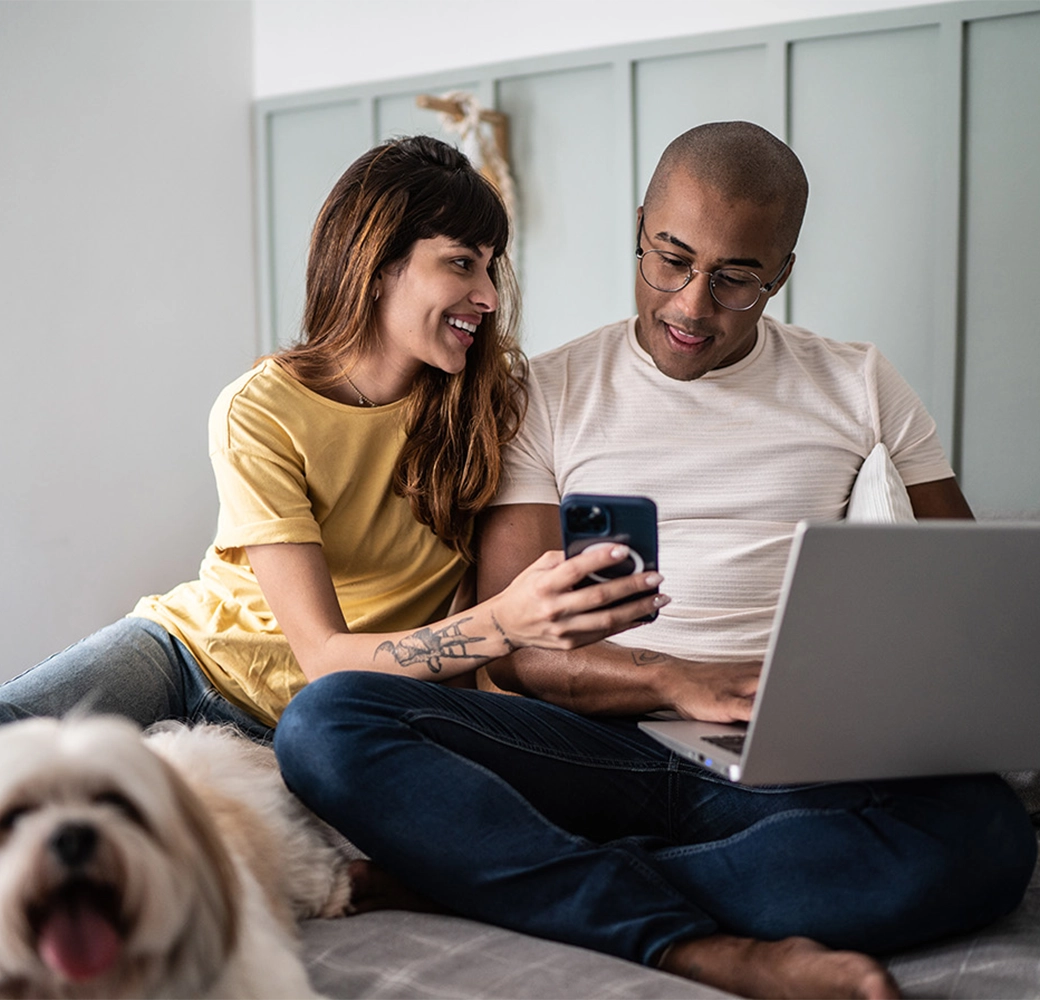 Couple looking at phone and computer with dog next to them